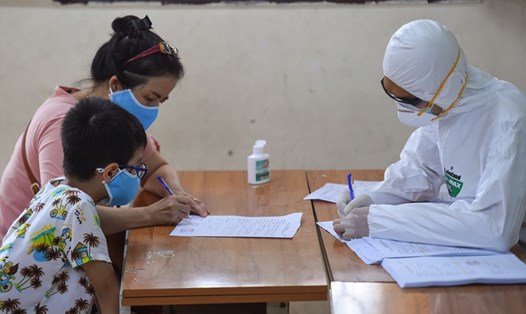 Nhân viên y tế ghi lại lịch trình di chuyển của người phụ nữ và bé trai tại một trung tâm xét nghiệm COVID-19 ở Hà Nội, ngày 8.8.2020. Ảnh: AFP
