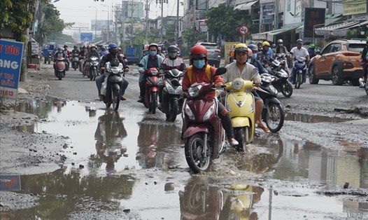 Người đi đường loạng choạng tay lái khi đi qua ổ gà ngập nước trên đường Lương Định Của.   Ảnh: Minh Quân