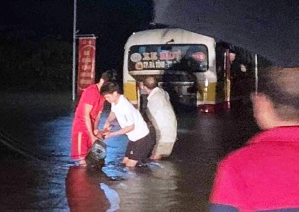 Người dân đang kéo móc từ xe cứu hộ vào vào để kéo xe bus thoát ra khỏi vùng ngập lụt. Ảnh: XH.