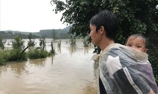 Một người dân xã Cư San, cõng con sau lưng, trùm áo mưa đứng lặng nhìn ra phía lòng hồ Krông Pách thượng - nơi nước lũ đang dâng cao sau bão số 12. Ảnh: Bảo Trung