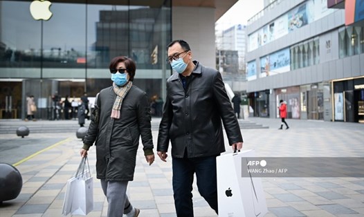 Một người đàn ông và một phụ nữ đeo khẩu trang bước ra khỏi cửa hàng Apple ở Bắc Kinh, Trung Quốc. Ảnh: AFP.