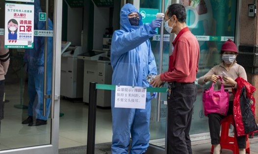 Nhân viên bảo vệ đo nhiệt độ của du khách tại lối vào một ngân hàng ở Quảng Châu. Ảnh: EPA-EFE.