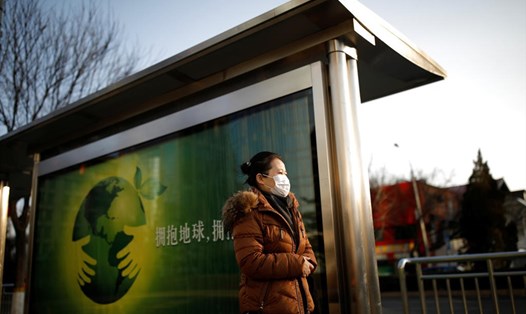 Một phụ nữ Trung Quốc đeo khẩu trang đứng chờ xe buýt ở Bắc Kinh. Ảnh: Reuters.