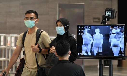 Cặp đôi đeo khẩu trang đi qua điểm kiểm tra nhiệt độ tại sân bay quốc tế Changi, Singapore. Ảnh: AFP.