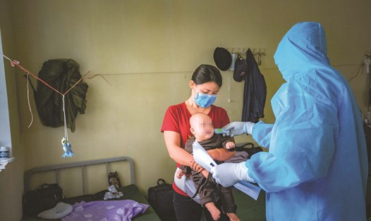 Cán bộ quân y đo thân nhiệt cho một cháu bé đang thực hiện cách ly cùng mẹ tại Trường Quân sự tỉnh Hoà Bình sau khi trở về từ vùng dịch Hàn Quốc. 
Ảnh: Lưu An Nhiên