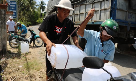 Nguyễn Thanh Phong (áo đen) đang giúp người dân xã Thới Lai (huyện Bình Đại, tỉnh Bến Tre) chở nước ngọt về nhà. Ảnh: L.H