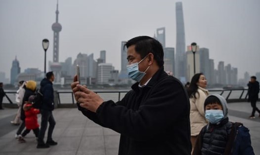 Một người đàn ông đeo khẩu trang chụp ảnh trên đường đi dạo dọc sông Hoàng Phố ở Thượng Hải. Ảnh: AFP.