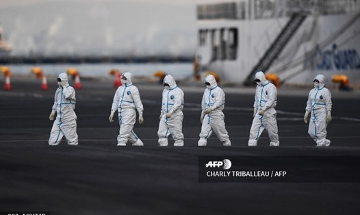 Những người mặc bộ đồ bảo hộ đi bộ từ tàu du lịch Diamond Princess - con tàu du lịch đầu tiên bùng phát dịch COVID-19 và bị cách ly ngoài khơi Nhật Bản. Ảnh: AFP