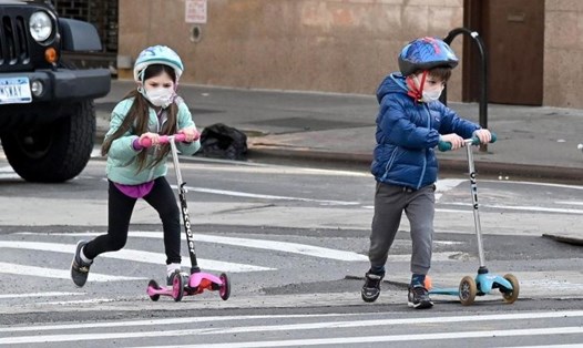 Hai em nhỏ đeo khẩu trang đang chơi xe trượt scooters trong khoảng thời gian dịch bệnh ở New York, 25.4. Ảnh: AFP
