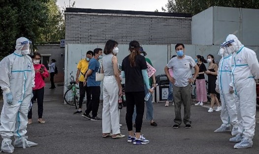 Các nhân viên y tế bên cạnh những người dân đeo khẩu trang xếp hàng chờ xét nghiệm COVID-19 ở Bắc Kinh, Trung Quốc ngày19.6. Ảnh: AFP