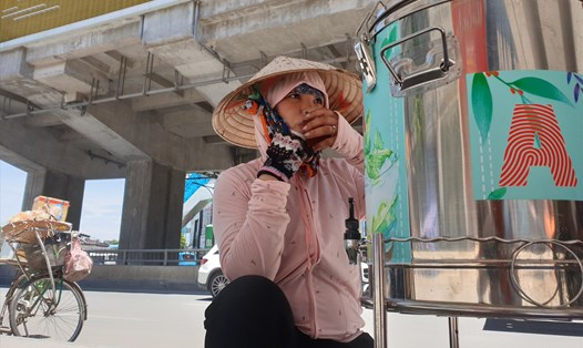 Chị Nguyễn Thị Lan uống nước giải nhiệt từ bình nước miễn phí trong thời tiết nắng nóng gay gắt. Ảnh: Phạm Đông
