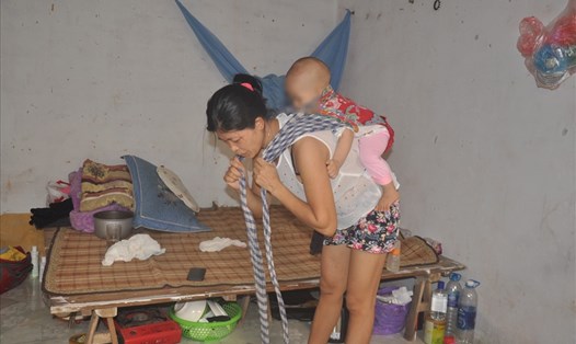 Trong căn phòng trọ tồi tàn, chị Trần Thị An địu con để chuẩn bị đi rửa bát thuê. Ảnh: Bảo Hân.
