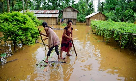 Hai cô gái trẻ đang sử dụng chiếc bè tự chế đi qua đoạn ngập lụt trong ngôi làng ở quận Karbi Anglong, tiểu bang Assam, Ấn Độ ngày 11.7. Ảnh: Reuters