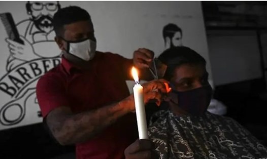 Một người đàn ông cầm nến khi cắt tóc ở Colombo, Sri Lanka vào ngày 17.8, thời điểm toàn quốc mất điện. Ảnh: AFP.