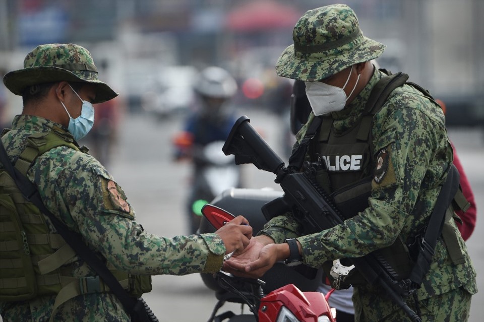Lực lượng có vũ trang khử trùng tay khi tiến hành kiểm tra danh tính tại một trạm kiểm soát ở Manila, Philippines khi lệnh tái phong tỏa được áp dụng từ 4.8. Ảnh: AFP.