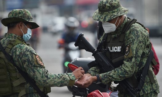 Lực lượng có vũ trang khử trùng tay khi tiến hành kiểm tra danh tính tại một trạm kiểm soát ở Manila, Philippines khi lệnh tái phong tỏa được áp dụng từ 4.8. Ảnh: AFP.