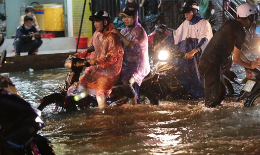 Người dân bì bõm lội nước trên đường Tô Ngọc Vân (Thành phố Thủ Đức) sau cơn mưa lớn tối 17.4. Ảnh: T.Q