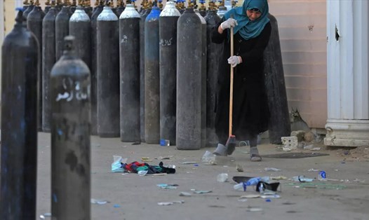 Một phụ nữ Iraq dọn dẹp các mảnh vỡ bên cạnh các bình ôxy bên ngoài bệnh viện Ibn al-Khatib ở Baghdad, Iraq vào ngày 25.4. Ảnh: AFP