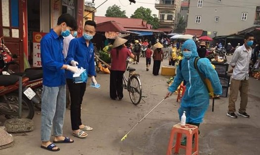 Lực lượng chức năng, đoàn thanh niên xã Dĩnh Trì (TP Bắc Giang) phun thuốc khử trùng và phát khẩu trang cho người dân tại chợ Cốc. Ảnh: BBG.