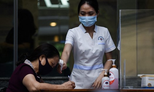 Nhân viên y tế đo thân nhiệt cho một phụ nữ điền vào tờ khai y tế bên ngoài bệnh viện ở Hà Nội hôm 5.5. Ảnh: AFP