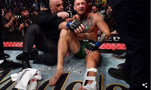 Conor McGregor ngồi bệt xuống sàn đấu, chấp nhận thua Dustin Poirier sau khi bị vỡ mắt cá chân ở cuối hiệp 1. Ảnh: Daily Mail.