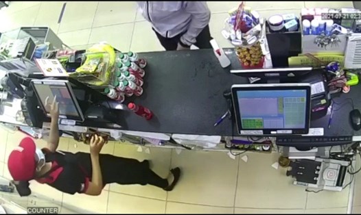Tên cướp (áo trắng đứng đối diện nữ nhân viên) vờ mua chai nước ngọt rồi rút dao từ túi quần. Ảnh: cắt clip