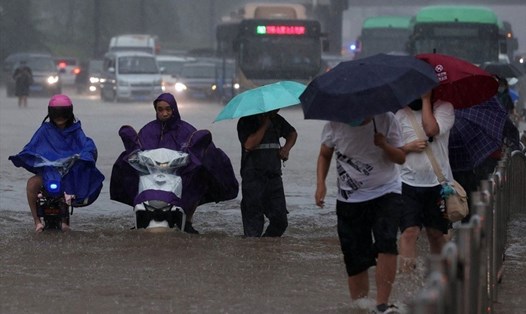 Người dân ở Trịnh Châu, Trung Quốc, đi qua dòng nước lũ trong mưa lớn. Ảnh: AFP