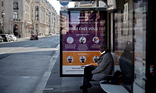 Một người đàn ông ngồi ở trạm xe buýt có tấm áp phích ghi "Hãy ở nhà" trên đường phố Paris ngày 1.4.2020. Ảnh: AFP