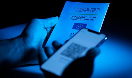 Màn hình điện thoại hiển thị mã QR và tờ giấy ghi chứng nhận COVID-19 kỹ thuật số EUDCC của Châu Âu. Ảnh minh họa. Ảnh: AFP