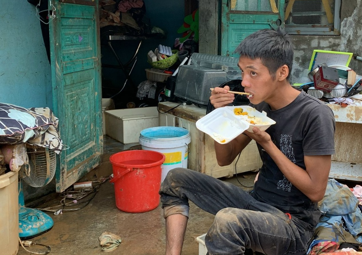 Anh Vũ lót dạ bằng suất cơm từ thiện giữa căn nhà ngổn ngang, tài sản hư hỏng hết vì mưa ngập. Ảnh: HVN