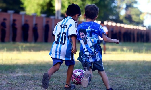Cổ động viên nhí Argentina với những chiếc áo gắn với hình ảnh Lionel Messi chơi bóng bên ngoài Trung tâm huấn luyện của Liên đoàn bóng đá Argentina. Ảnh: AFA