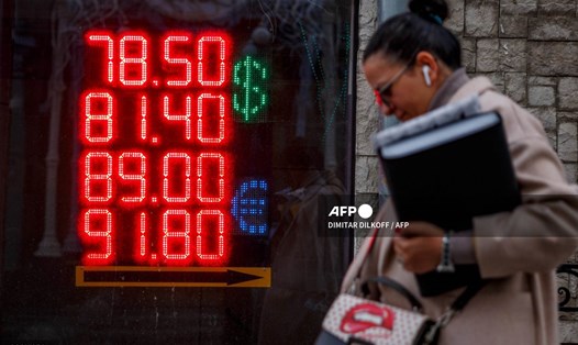Một người phụ nữ đi ngang qua bảng hiển thị tỉ giá hối đoái của đồng USD và đồng euro so với đồng rúp của Nga ở Mátxcơva ngày 22.2.2022. Ảnh: AFP