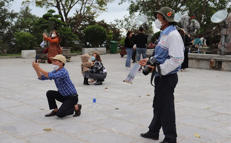 Ông Ánh  bất lực nhìn du khách chụp hình tại chùa Linh Ứng Bãi Bụt (Đà Nẵng) bằng điện thoại thông minh thay vì sử dụng dịch vụ chụp hình lấy liền của ông. Ảnh: Nguyễn Linh