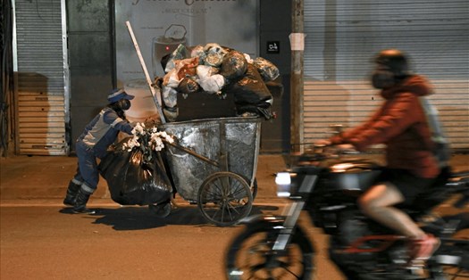 Những người công nhân lặng lẽ đẩy xe rác nặng nề trong đêm tối.