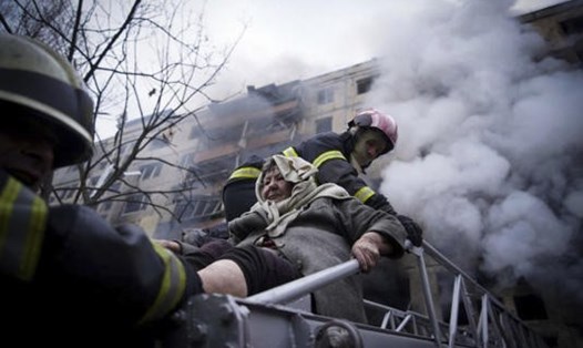 Lính cứu hỏa Ukraina sơ tán một cụ bà khỏi căn nhà ở Kiev vừa trúng pháo kích ngày 14.3. Ảnh: AFP