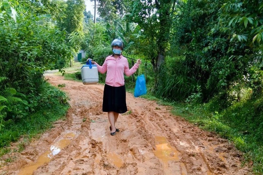 Chị Nguyễn Thị Thuỷ đi lấy mẫu xét nghiệm trên con đường lầy lội. Ảnh: Mạnh Đạt