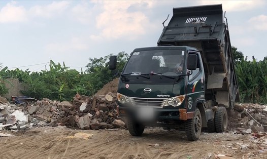 Xe tải chở phế thải xây dựng đổ xuống các hố chôn lấp trên đất bãi bồi ven sông Hồng. Ảnh: PV