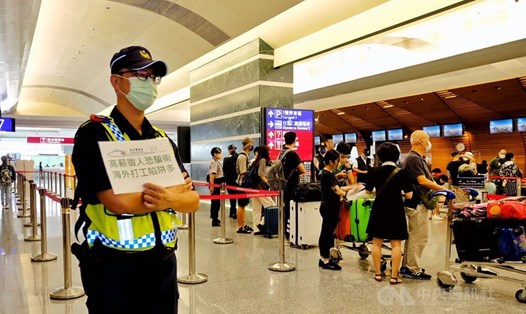 Cảnh sát cầm biển cảnh báo hành khách về các vụ lừa đảo việc làm tại sân bay quốc tế Đào Viên, Đài Loan (Trung Quốc) ngày 18.8.2022. Ảnh: CNA