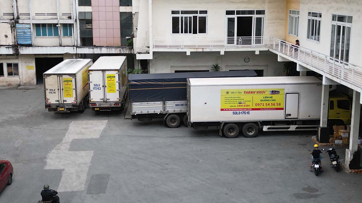 Có 3 xe tải vận chuyển hàng hoá của Thành Bưởi đỗ trong khu đất này.