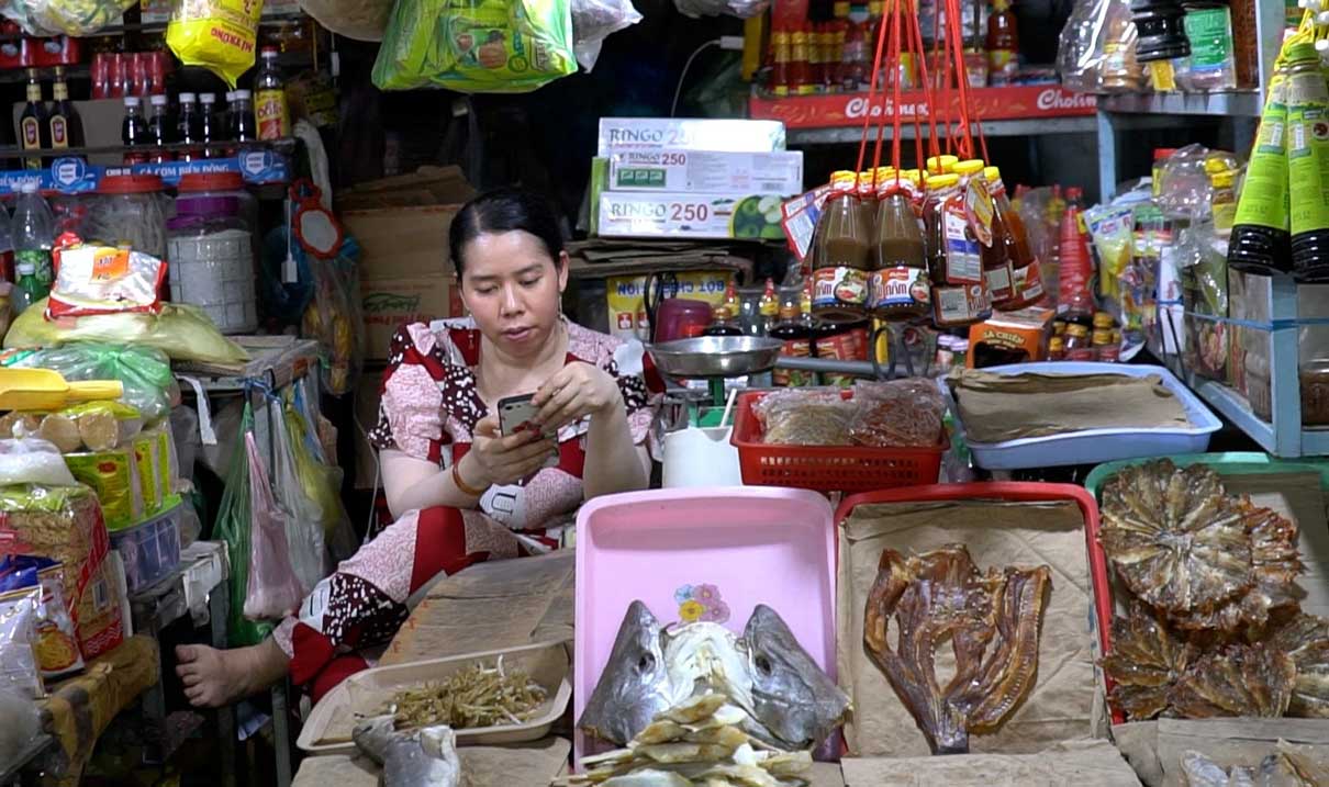Bấm điện thoại là cách tiểu thương giết thời gian khi buôn bán ế ẩm. Ảnh: Mỹ Ly