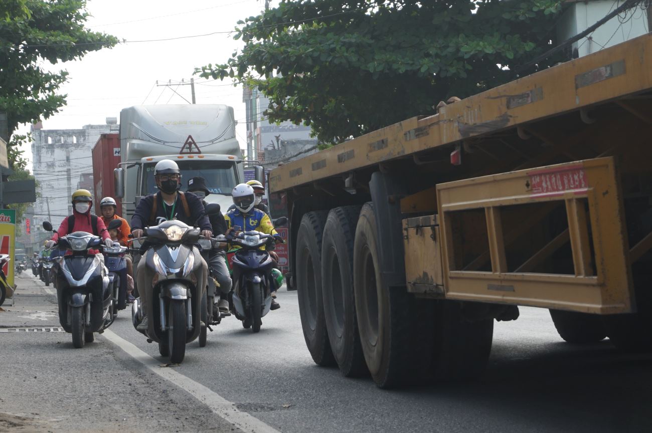 Người đi đường len lỏi sau xe container trên đường Nguyễn Duy Trinh.  Ảnh: Minh Quân