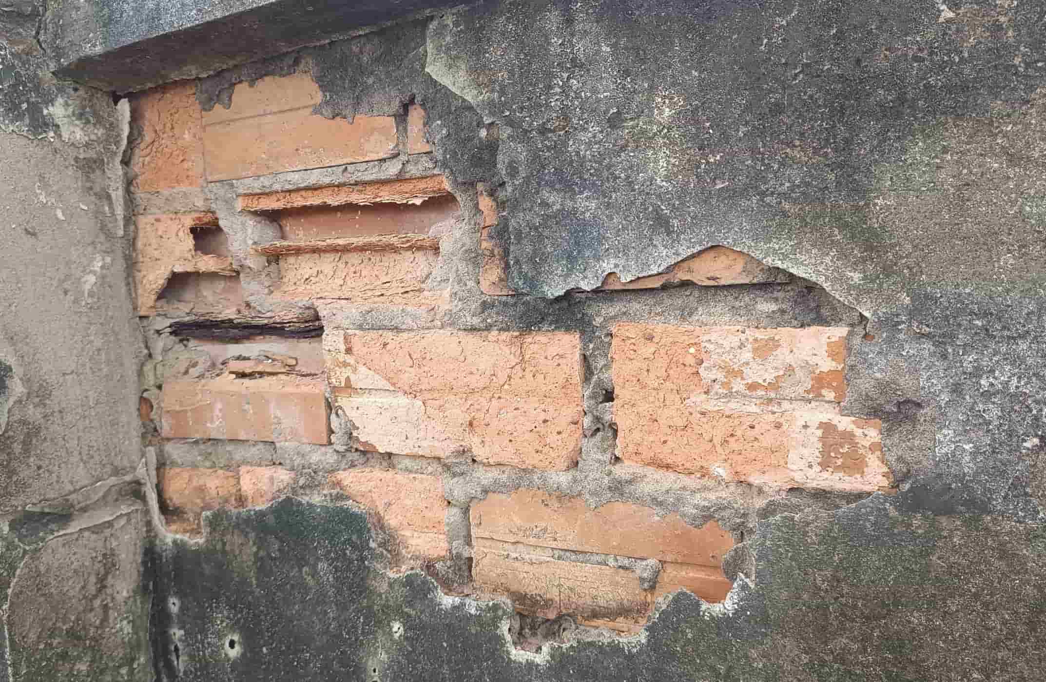 Nhiều mảng tường bị bong tróc, lớp vôi vữa bên ngoài rơi vỡ gạch bị xói mòn.