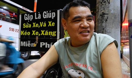 Anh Nguyễn Thành Nhân ngồi trên vỉa hè cùng tấm biển "Gặp là giúp, sửa xe, vá xe, kéo xe, xăng miễn phí".  Ảnh: Phương Uyên