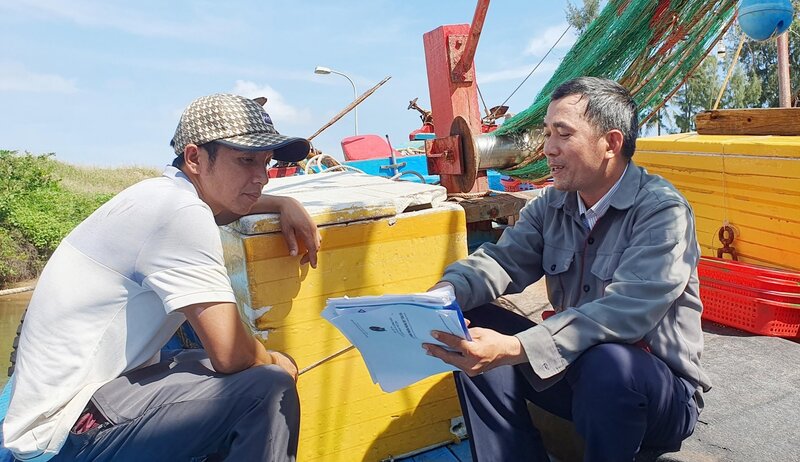 Cán bộ Trung tâm Đăng kiểm tàu cá tỉnh Quảng Ngãi hướng dẫn ngư dân xã Nghĩa An, TP Quảng Ngãi làm giấy tờ đăng kiểm cho tàu cá. Ảnh: Ý Thu
