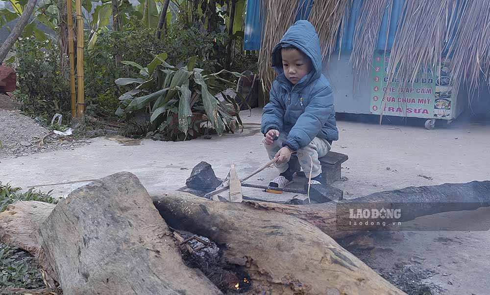 Một đứa trẻ được mẹ đốt lửa cho ngồi sưởi ấm để chống lại cái lạnh đầu mùa. 