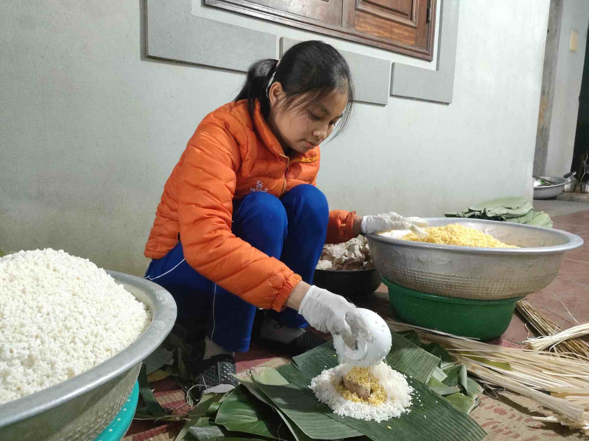 Chị Thương (34 tuổi, con dâu bà Nguyễn Thị Dâng) sáng đi dạy học, chiều về phụ mẹ gói bánh chưng. Ảnh: Mai Dung