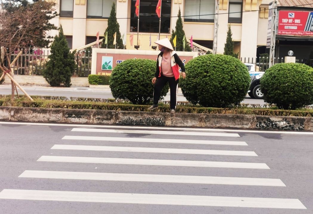 Một người phụ nữ phải leo lên dải phân cách giữa đường rồi chui qua hàng cây để đến chỗ kẻ vạch dành cho người đi bộ tại nút giao Nguyễn Lương Bằng - Nguyễn Đại Năng, TP.Hải Dương. Ảnh: Hoàng Thông