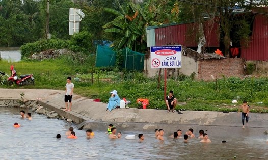 Người dân vô tư cho con trẻ vui chơi, bơi lội ở cống Mỹ Khê bất chấp biển cấm nguy hiểm. Ảnh: Băng Tâm