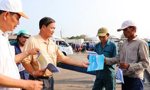 Ông Nguyễn Trính (người thứ hai từ trái qua) phát các tờ rơi tuyên truyền cho ngư dân. Ảnh: Thành An