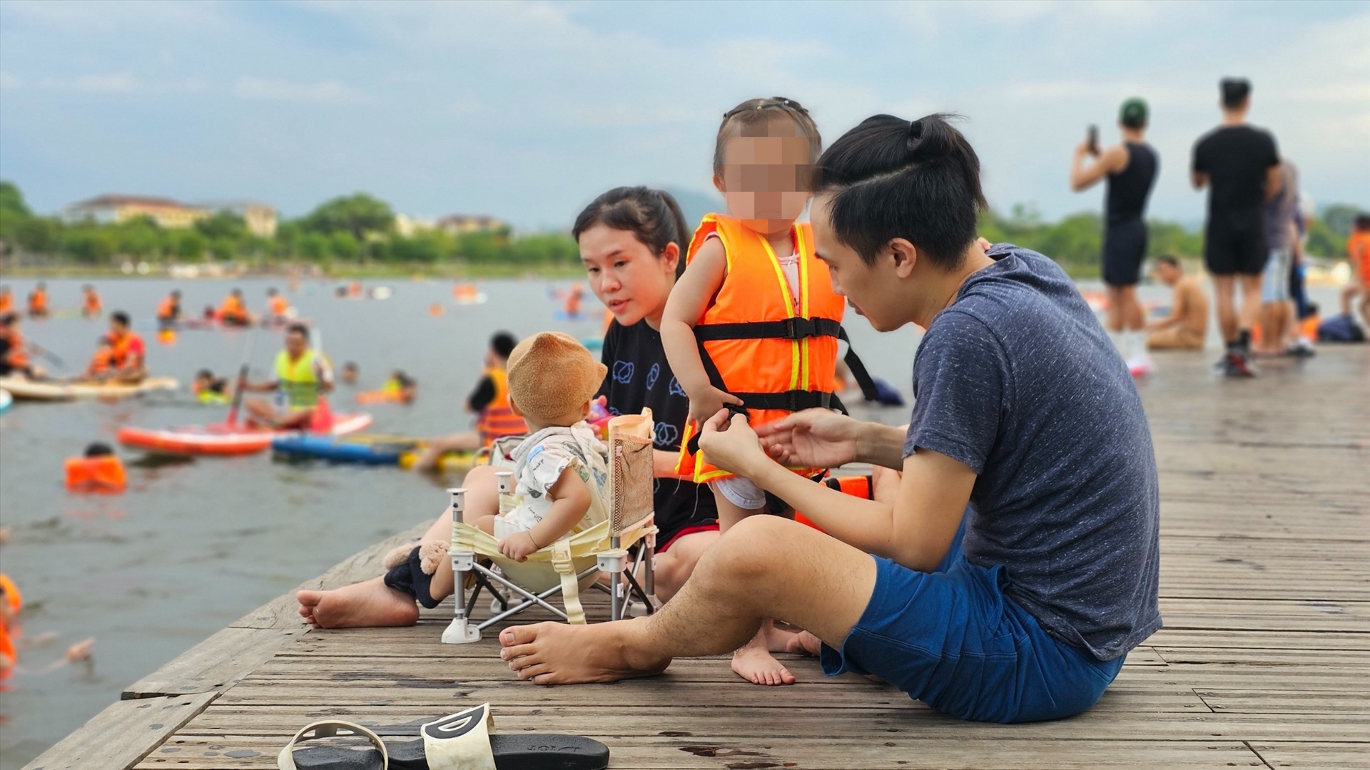Trên cầu Bán Nguyệt, một gia đình nhỏ đang chuẩn bị áo phao, khởi động trước khi xuống nước.